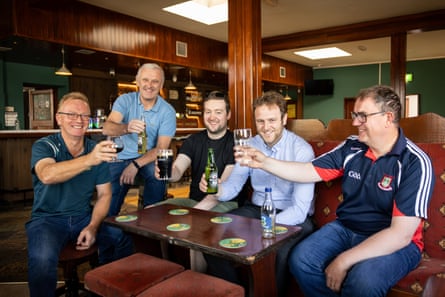 Six men of varying ages, all casually dressed, sit around a table in the traditionally furnished pub and raise their glasses or bottles.
