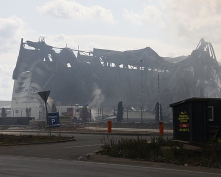 A fire engine outside a large, destroyed warehouse