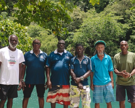 A group of men standing in front of blue water with green trees in the background