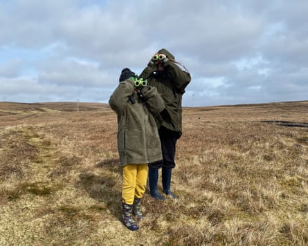 Two children standing holding binoculars up to their eyes so their faces can’t be seen