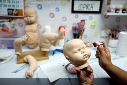 a hand holds a lifelike baby doll head at work table with other parts of the doll