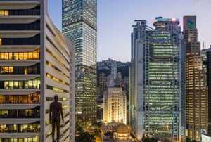 As evening falls, the lights in Hong Kong's skyscrapers  start to come on. Towards the left of the shot is the silhouette of a naked man sculpture by Antony Gormley, seeming to gaze across the illuminated skyline.