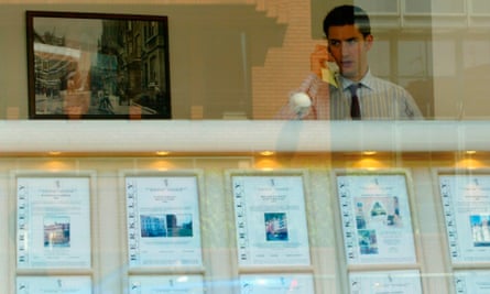 An estate agent talks on the phone behind a window display of properties for sale