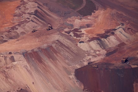 Huge dumper trucks appear tiny amid a vast ochre-coloured open-pit mine 