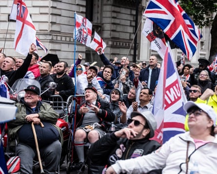Crowd of people smile, cheer, raise their fists and wave British flags