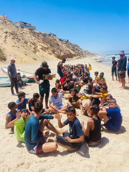 Children sitting on the beach and waving at the camera