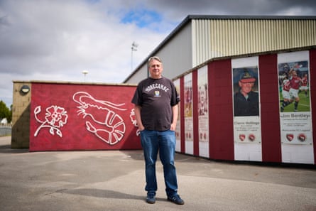 Mike Gibson stands with hands in pockets next to a shrimp logo and tributes to past players on a wall outside the club