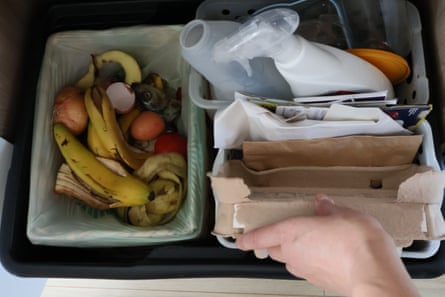 A top-down view of an open bin. The bin is divided into sections. Woman hand reaching into the binA top-down view of an open recycling bin. The bin is divided into sections, each containing different types of recyclable materials. There is a hand in the frame, reaching into the bin.