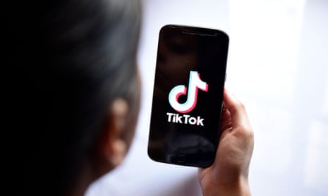 A woman looking at a phone with the TikTok logo