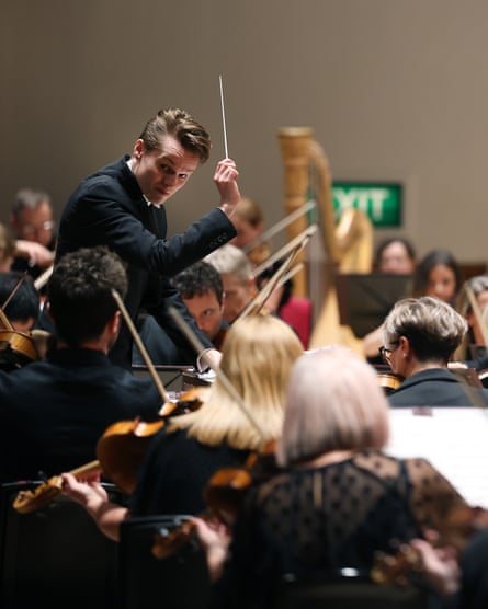 Conductor Adam Hickox raises a baton while leading an orchestra of string musicians