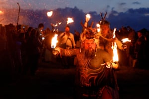People dressed in historical tribal costumes, including deer antlers on their heads, hold fire torches