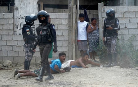 Two youths lie face down in the dirt outside a breezeblock house in a poor area as soldiers stand over them