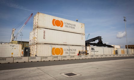 A stack of three shipping containers outside, painted cream with an orange logo