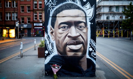 Mural of the head of George Floyd painted by Akse on a wall on a street in Manchester with a bouquet of flowers propped up underneath
