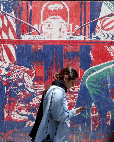 A girl walks past a large mural with US and Iranian flags and symbols