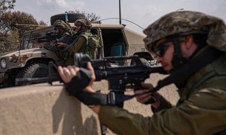 Two soldiers standing next to a miltary vehicle in the background and another soldier with an assault rifle in the foreground 