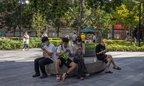 Young Chinese people use their mobile phones as they sit in the shopping and residential area of Sanlitun, in Beijing