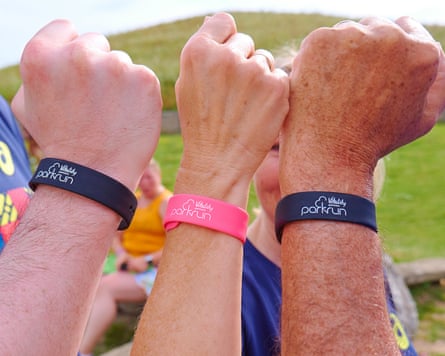 Three people hold up their arms, showing parkrun wristbands on their wrists.
