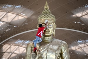 A worker cleans a large statue of Buddha