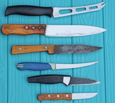 A set of different old coloured table knives lie on a blue wooden table