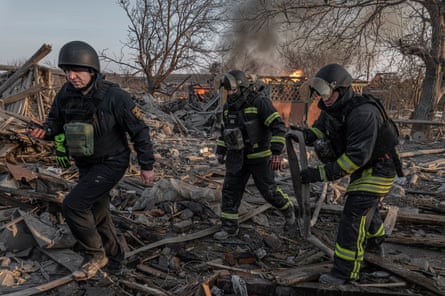 Firefighters moving through the burnt remains of trees and buildings
