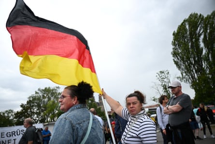 Two women in foreground, one holding a German flag fluttering in wind.