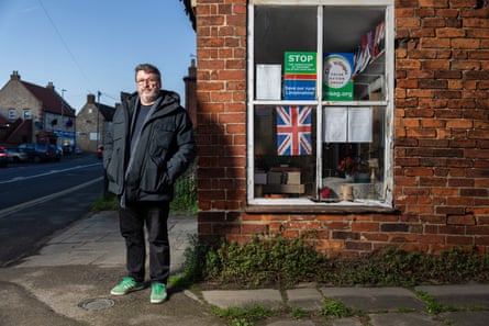 Labour councillor Neil Murray who supports the use and installation of more solar farms in Lincolnshire, UK, outside a village shop that displays anti-solar farm signs
