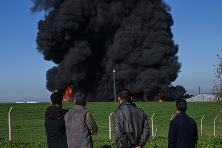 People watch as black smoke billows from an oil warehouse