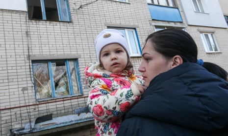 A woman holds a young girl outside a damaged residential building.