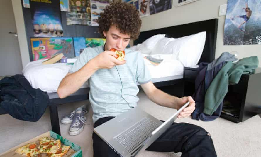 Băiat adolescent așezat pe podeaua dormitorului cu laptop și pizza