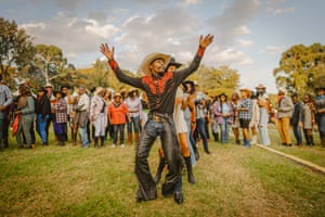 A man in a cowboy hat and black shirt with red detailing dances with his hands in the air