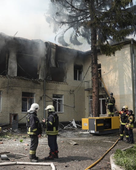 Rescuers in front of the kindergarten, which has burnt-out windows and smokes rising from it