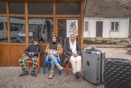Selma Ghasemzadeh sits with her mother and brother in plastic chairs near large suitcases