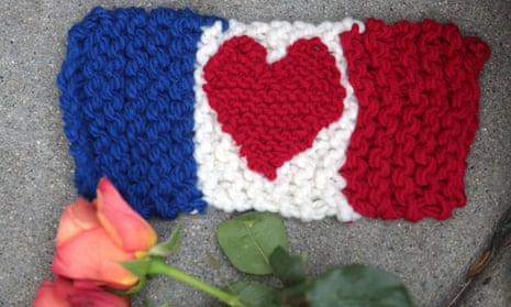 A knitted French flag with a heart design lies beside a rose on the pavement outside the French consulate in Boston, USA