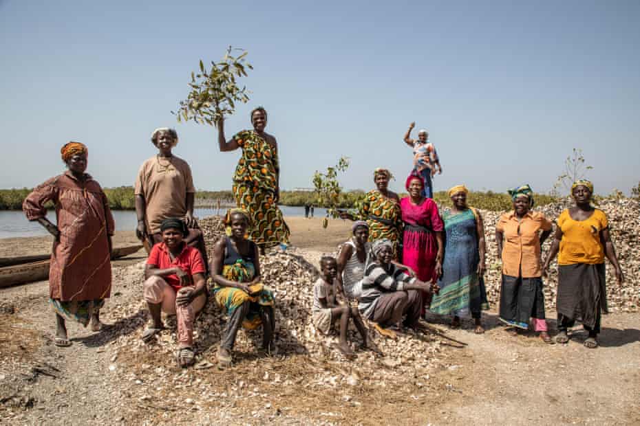 13 mulheres e uma criança posam para a câmera perto do rio Gâmbia em meio a montes de conchas de ostras