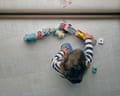 A curly haired toddler sitting on floor near window and playing with toy cars and train