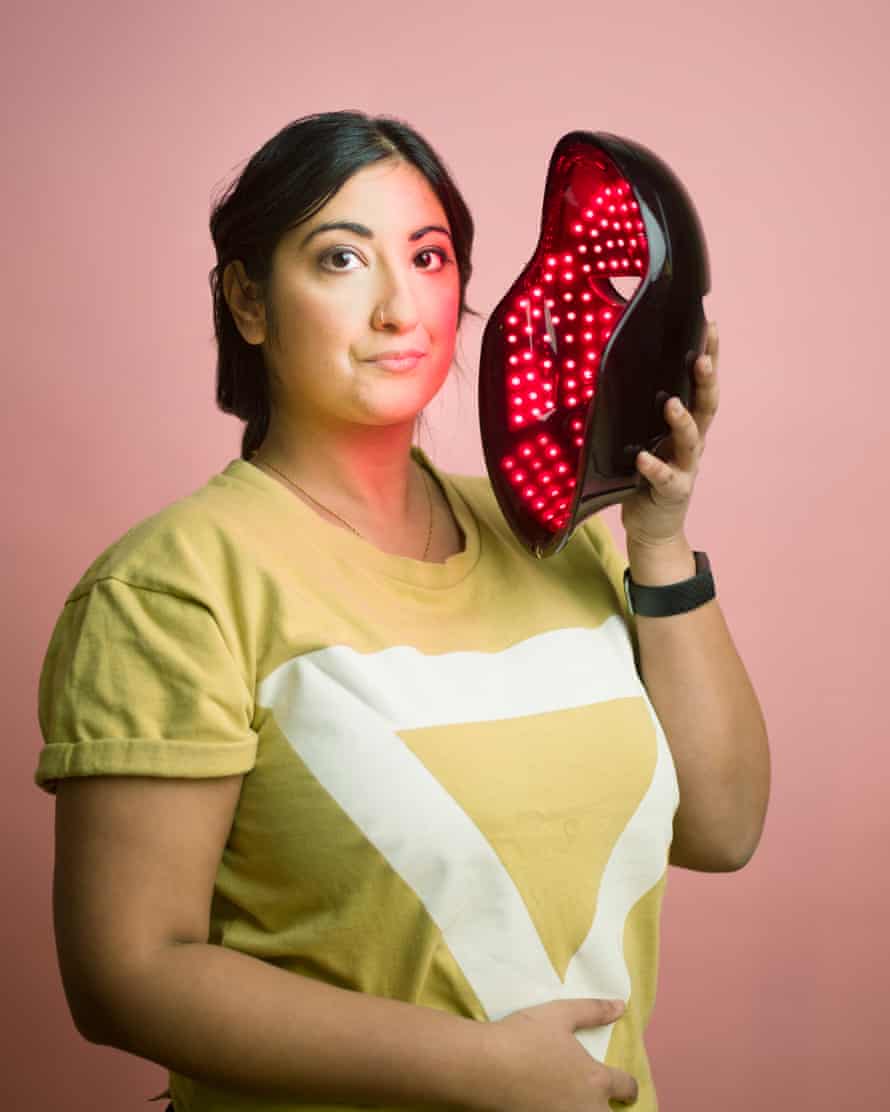 Guardian writer Coco Khan holding an LED face mask, against a pink background
