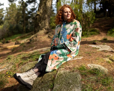 Maggie O'Farrell sits on a rocky outcrop in a forest wearing a colourful painted coat
