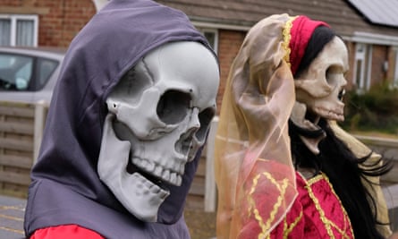 Two mannequins wearing skull masks sitting by a garden walls
