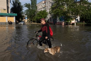 A local resident with a bike and a dog walks along flooded streets past the buildings in Kherson.