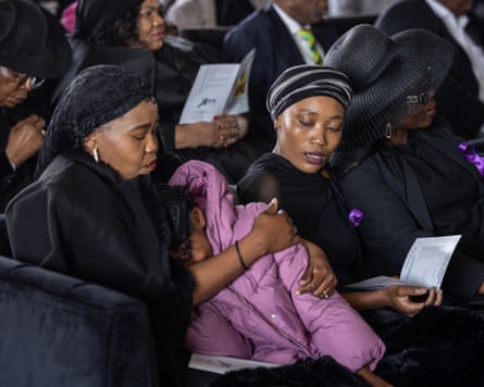 Two women in black mourning outfits comfort a young girl in a pink padded jacket