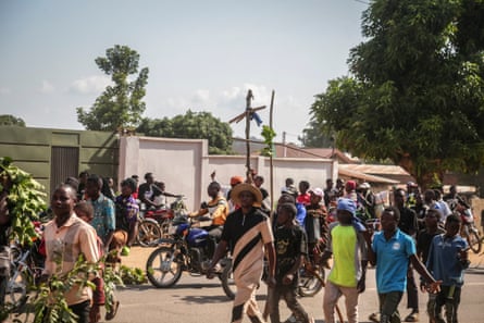 A crowd of people walk or ride motorcycles along a road, two of them holding up makeshift wooden crosses