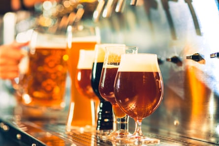 A row of various coloured and shaped beers settling in the glasses beneath the beer tap