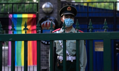 Een Chinese paramilitaire politieagent met masker op staat buiten de Zweedse ambassade, waar een Pride-spandoek hangt.