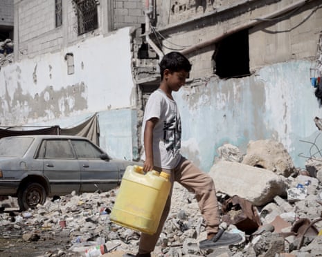 A Palestinian child living in an accommodation centre carries a canister amid the rubble of collapsed buildings in Khan Younis, Gaza on 08 October 2025.