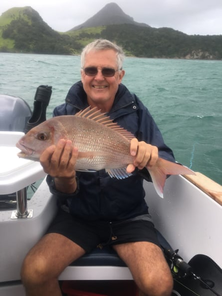 Terry Strong hält auf einem Boot einen Fisch hoch und lächelt