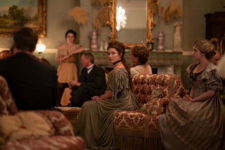 Florence Pugh sits on a sofa in a richly decorated room, surrounded by other cast members