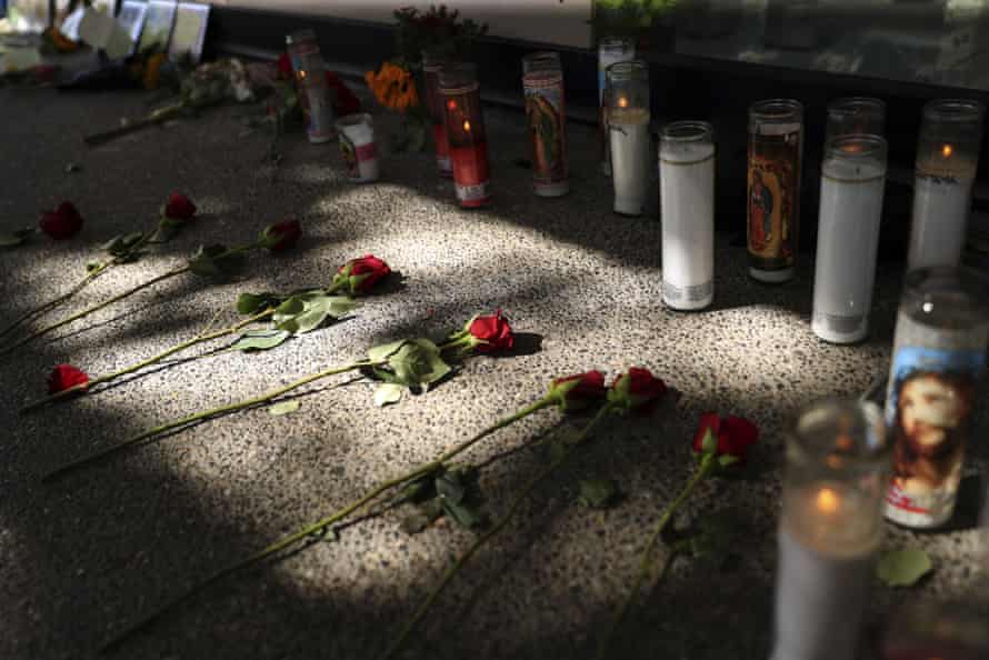 Eight red roses lay on the pavement near a cluster of candles that serves as a memorial site.