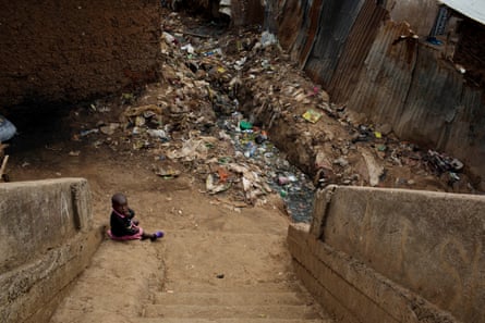 A young baby sits alone at the bottom of some stairs surrounded by litter in Kibera, Nairobi.