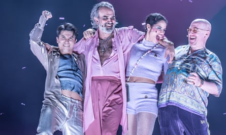 Gerald Kyd as Don Pedro wearing pink trousers, shirt and long jacket. He has his arms around two other cast members, as another stands alongside
